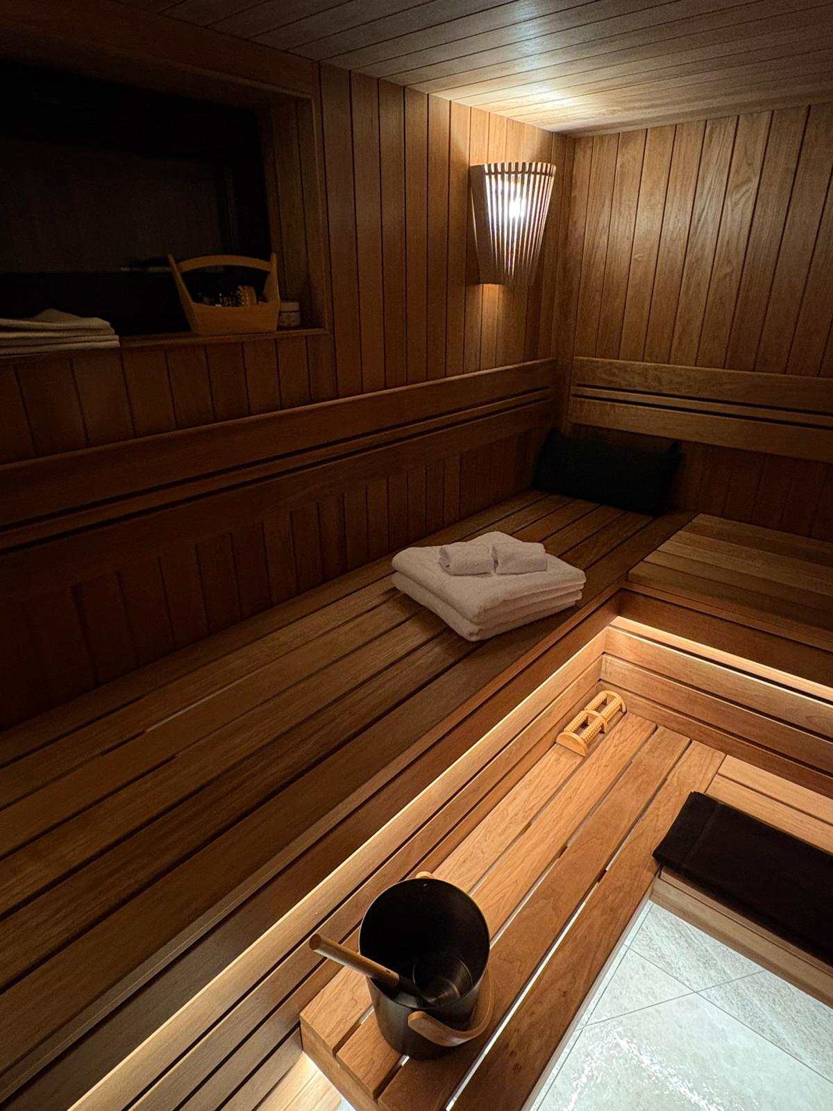 Beautiful wooden sauna interior with warm lighting, bench, towels and traditional bucket